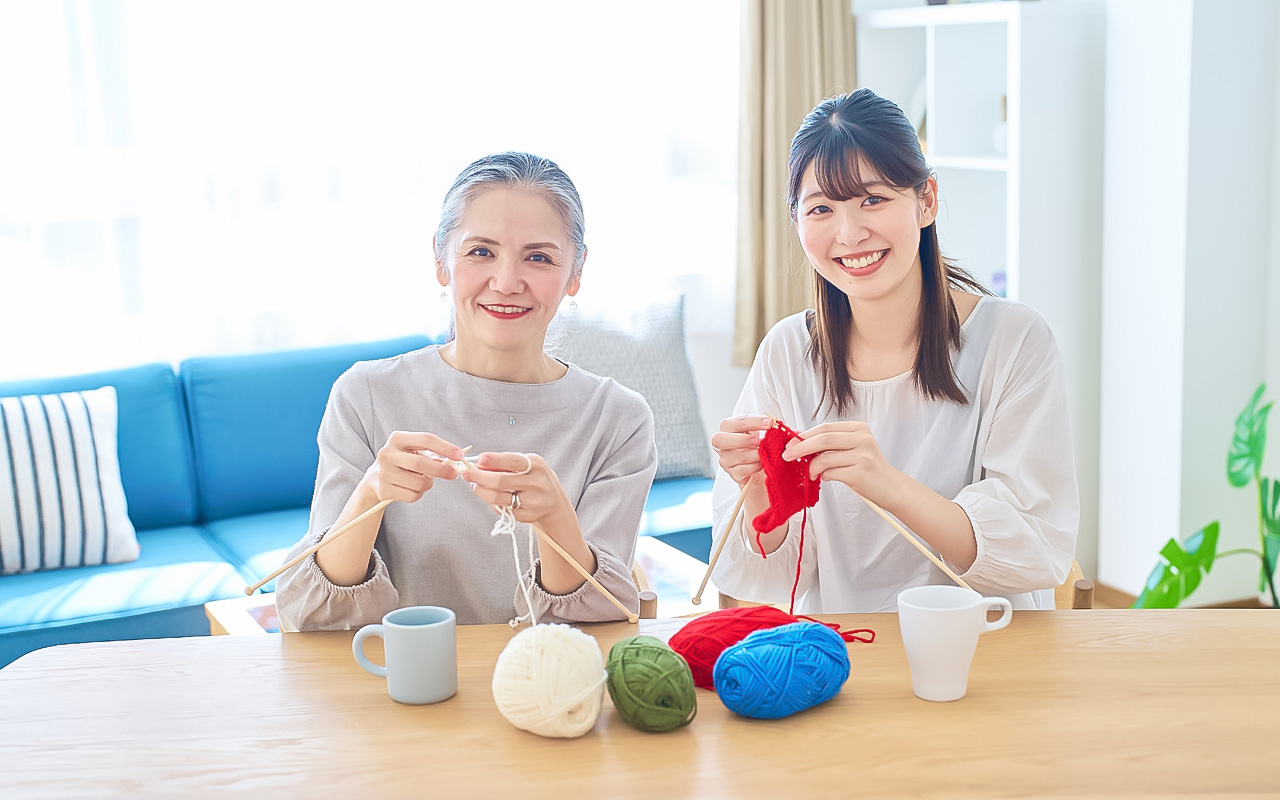 編み物をしながら微笑むシニア女性と施設スタッフの女性
